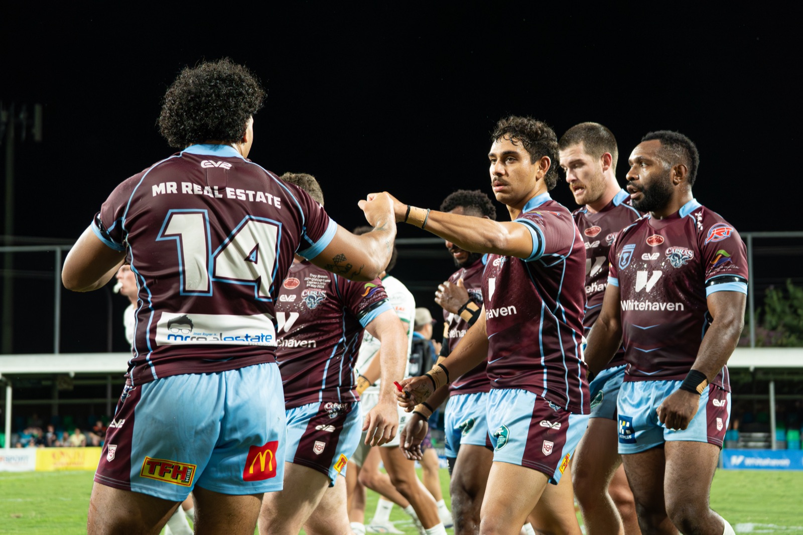 Capras players fist-bumping on field mid-game, sponsor logos visible on jerseys